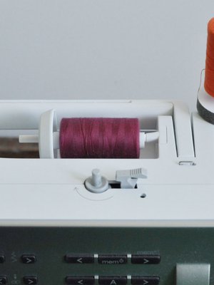 Aseta lankarullat ompelelukoneen tappeihin. HUOM! Valitse oikeaan ty&ouml;h&ouml;n kankaan v&auml;riset langat.