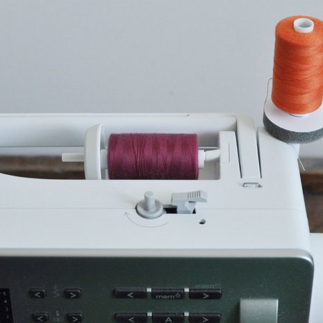 Aseta lankarullat ompelelukoneen tappeihin. HUOM! Valitse oikeaan ty&ouml;h&ouml;n kankaan v&auml;riset langat.