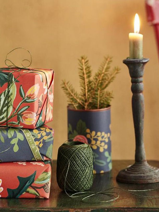 Tänä vuonna kuusen alta pilkottaa täyteläisiä värejä ja kukkakuoseja. Kuusiruukku syntyi päällystämällä peltipurkki lahjapaperilla. Rifle Paper -kukkapaperit Papershop, paperinaru Askarelli, peltipöytä Moko ja kynttilänjalka Mosa Interiors.