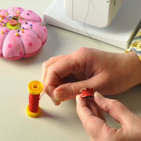 Tarvitset kankaan v&auml;riin sopivaa ompelu- ja kumilankaa. Kieputa kumilanka k&auml;sin ompelukoneen puolalle. Pid&auml; lanka kire&auml;n&auml; puolatessasi.