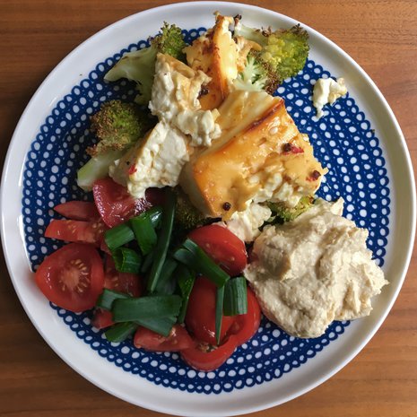 Lautasellinen täydellisiä makuja: paahdettua fetaa ja parsakaalia, hummusta, tomaattia ja sipulinvarsia. Kokeile satsia myös pitaleivän täytteeksi!