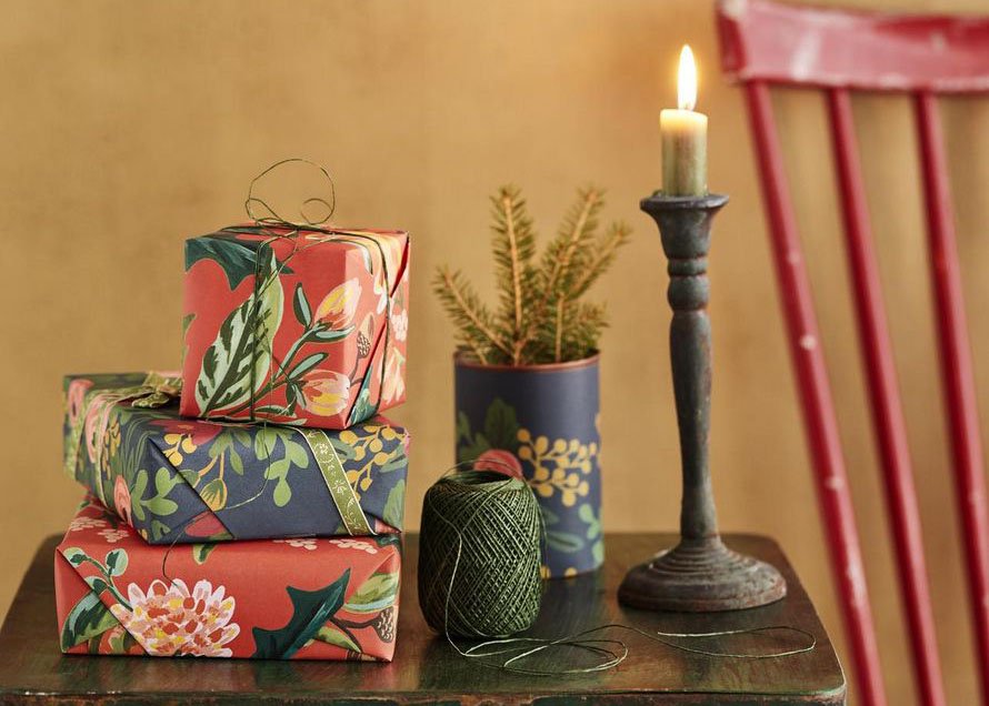 Tänä vuonna kuusen alta pilkottaa täyteläisiä värejä ja kukkakuoseja. Kuusiruukku syntyi päällystämällä peltipurkki lahjapaperilla. Rifle Paper -kukkapaperit Papershop, paperinaru Askarelli, peltipöytä Moko ja kynttilänjalka Mosa Interiors.