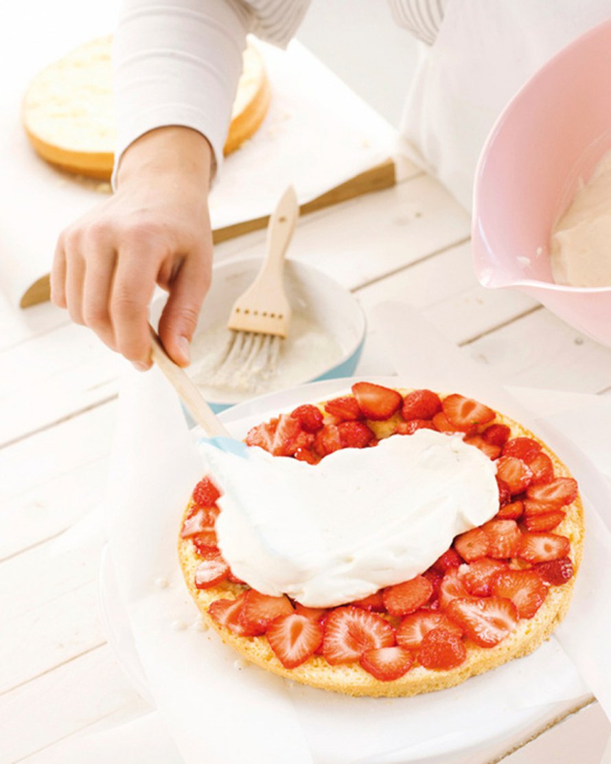 Leikkaa jäähtynyt kakku kolmeen osaan. Levitä pohjalle puolet mansikan viipaleista ja näiden päälle puolet kermarahkasta.