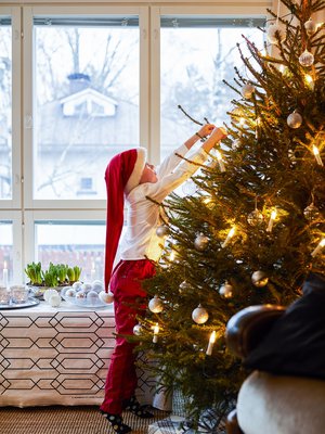 Erjon perheen kuusi on perinteisesti aito ja niin suuri kuin olkkariin sopii. Eemil auttaa äitiä koristelemaan kuusta hopeanvärisillä ja lasisilla palloilla.