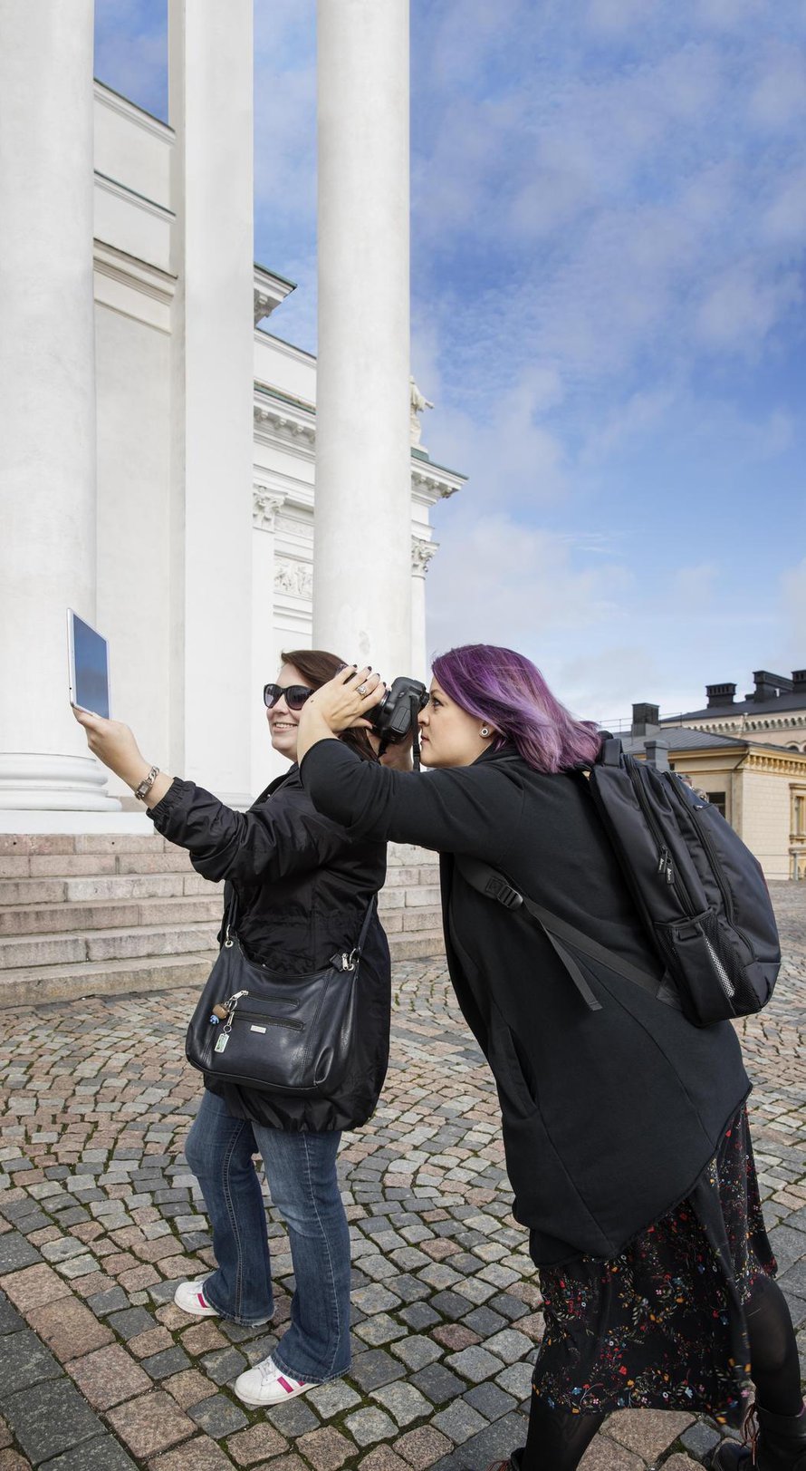 Näin syntyy blogipostaus. Satu pitelee tablettia, jolla näkyy pysäytyskuva elokuvasta. Tiia ottaa kuvan, jossa tabletin kuva istuu täydellisesti taustaan.